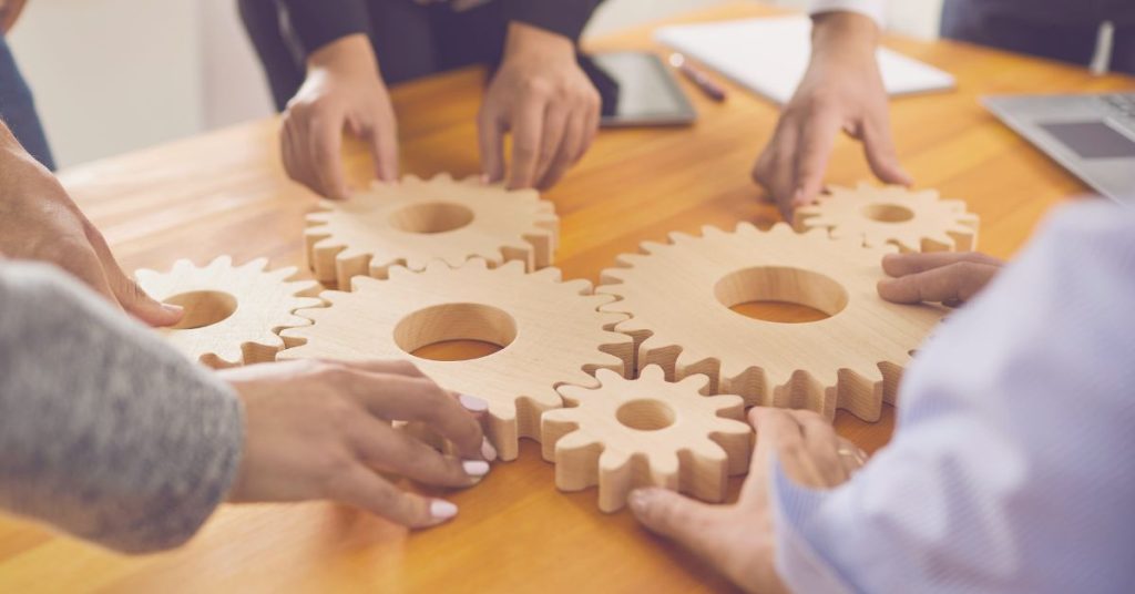Driving Innovation Through Inclusion: Diverse hands holding interconnected wooden gears on a table.